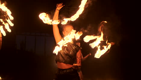 Drei-Frauen-Mit-Brennenden-Reifen-Tanzen-Mit-Feurigen-Fackeln-In-Lederkleidung-In-Einem-Dunklen-Hangar-Und-Demonstrieren-In-Zeitlupe-Eine-Zirkusfeuershow